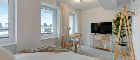 A modern hotel room with a large bed, a desk with a chair, a television, and a plant.