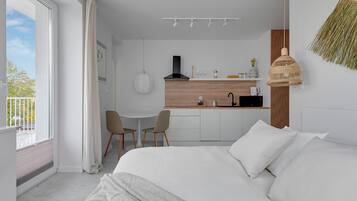 A modern hotel room with a large bed, a dining area, and a kitchen.