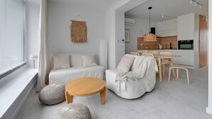 A modern living room with a sofa, a round wooden coffee table, and a dining area with a table and chairs.