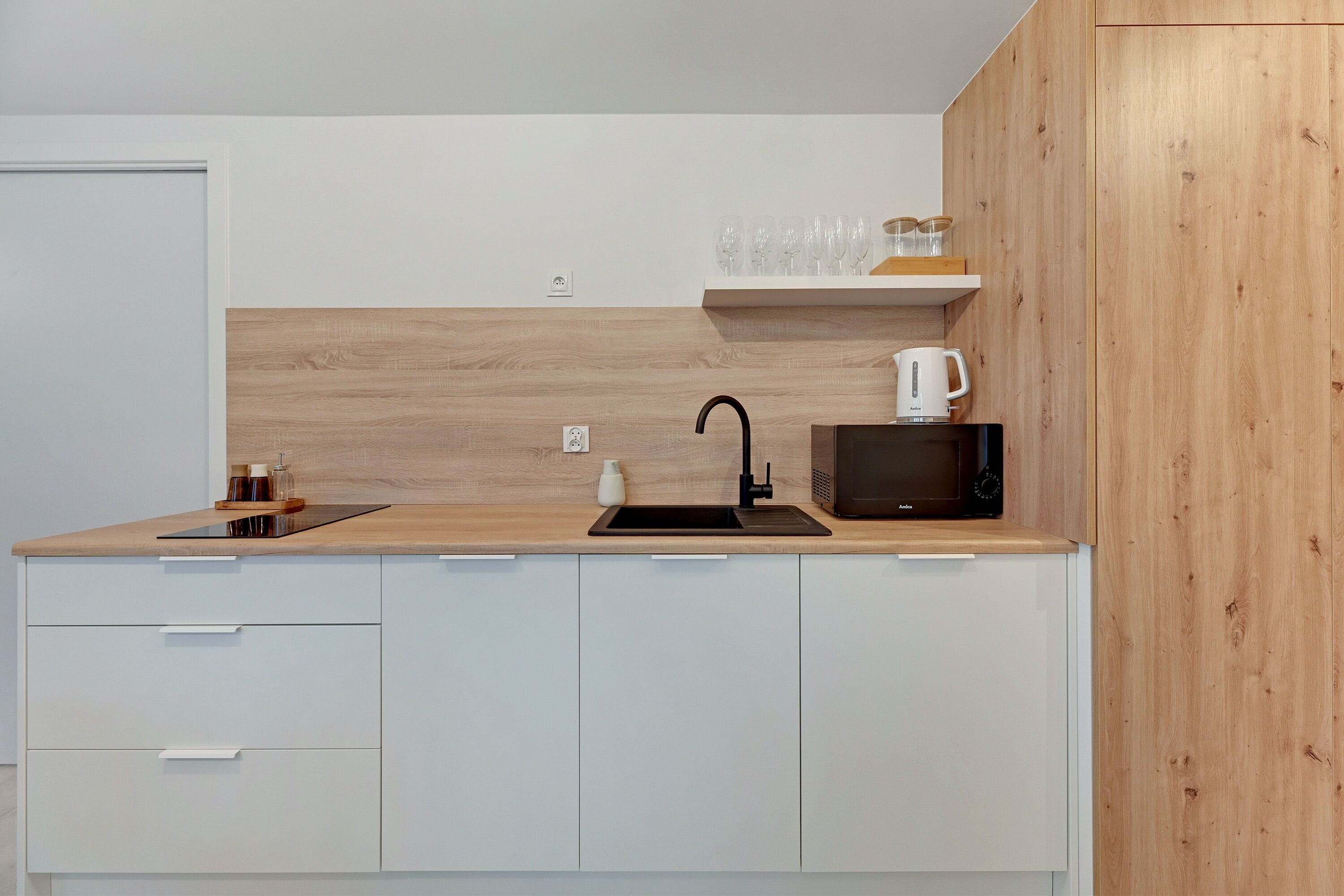 Una cocina moderna con encimera de madera, un fregadero, un microondas y una estantería con vasos y frascos.