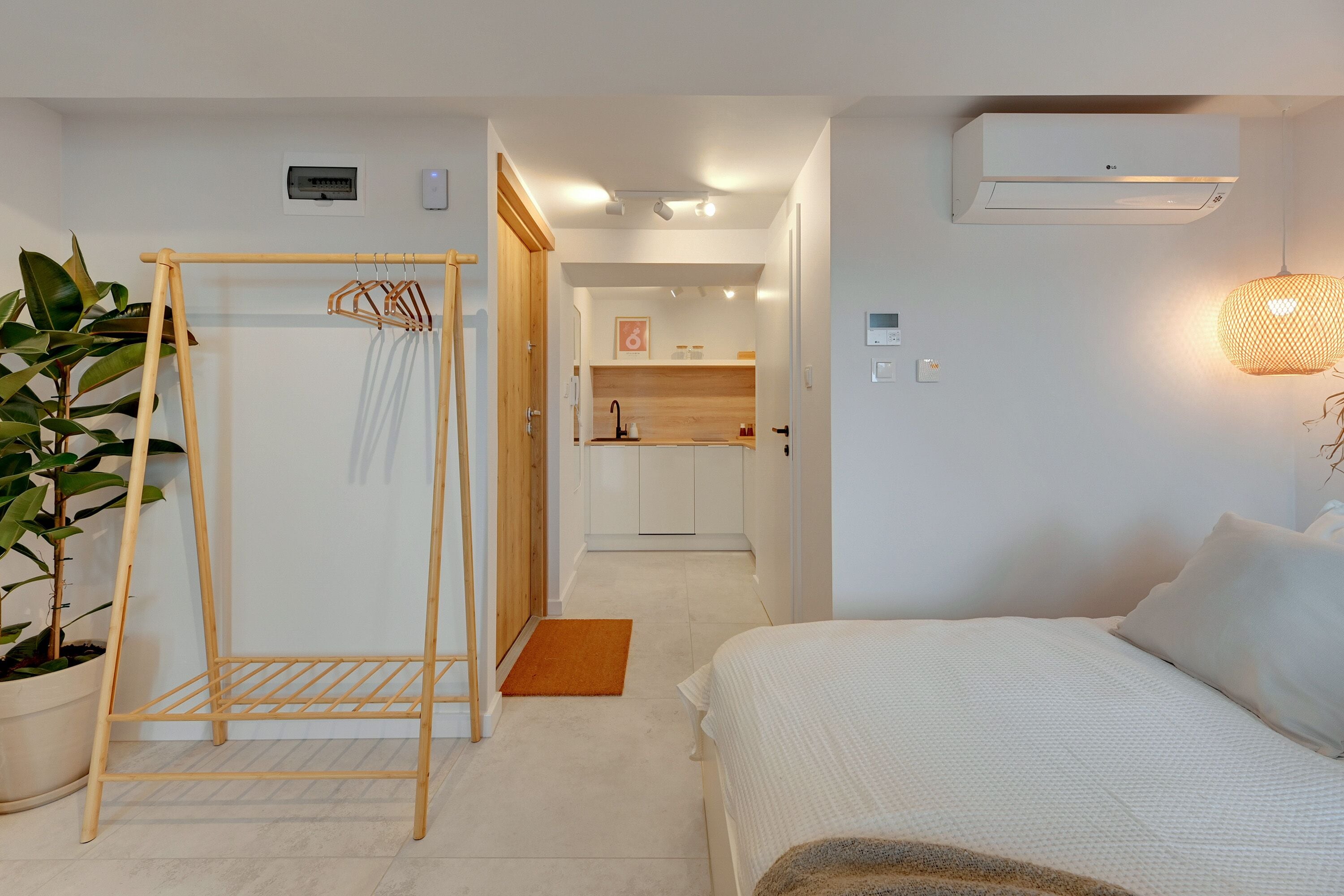 Un dormitorio con cama, un tendedero de madera, una planta en maceta y un equipo de aire acondicionado.