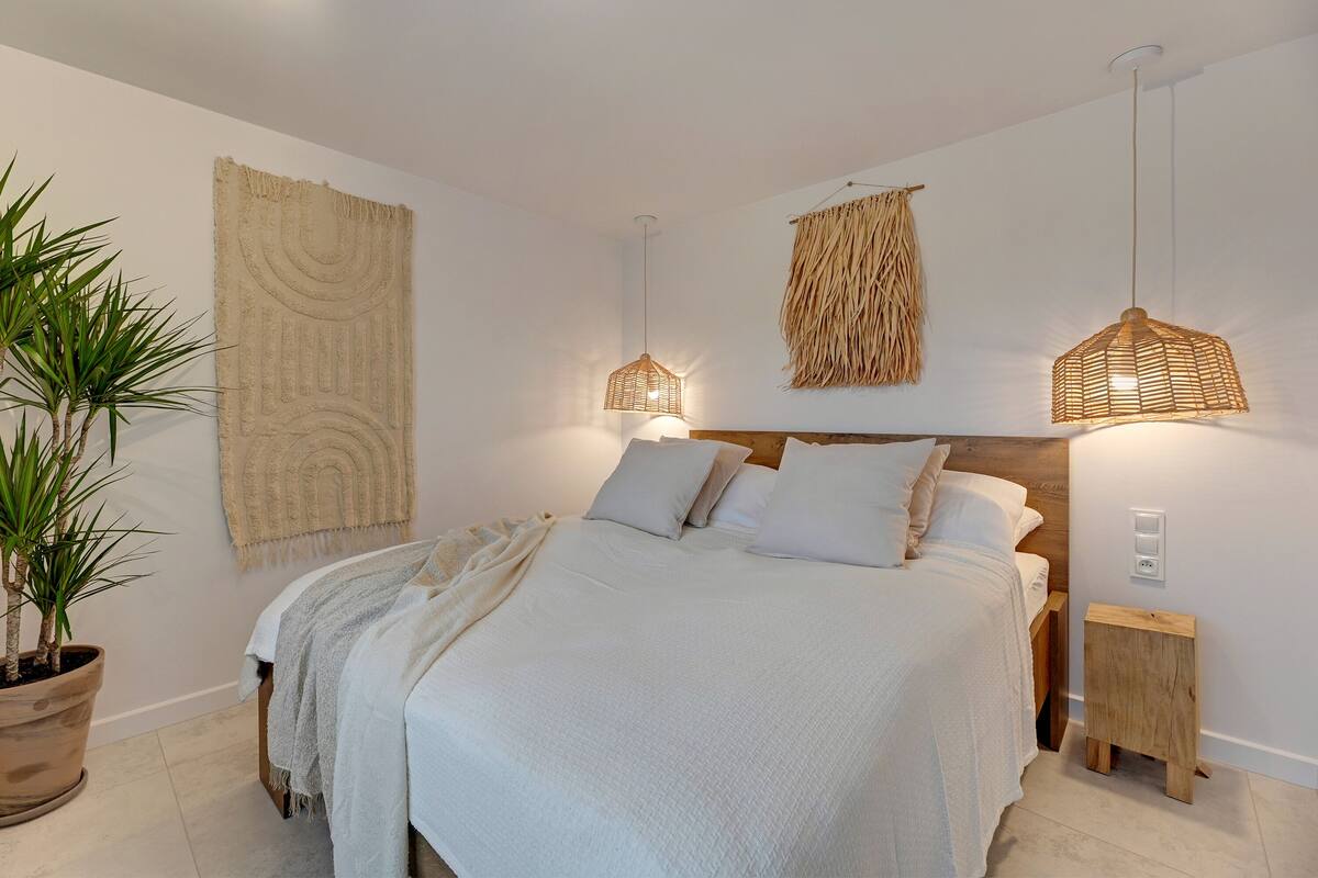Een slaapkamer met een groot bed, twee nachtkastjes, een potplant en wanddecoraties.