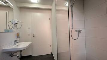 Ein modernes Badezimmer mit einem weißen Waschbecken, einer Glasdusche und einer Tür zu einem anderen Raum.