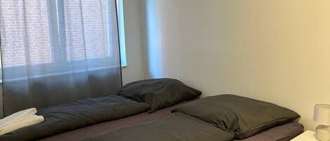 Una habitación con una cama, una mesita de noche y un ventanal con cortinas.