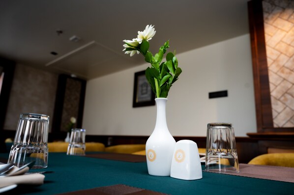 A dining table with a white vase and salt and pepper shakers, a green tablecloth, and clear glasses.