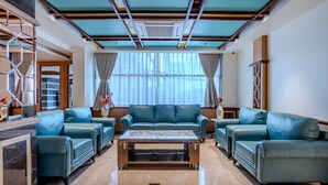 A spacious living room with teal leather sofas arranged around a central coffee table, a marble floor, and a large window with sheer curtains. - HOTEL LUCKY INDIA  (Bhubaneshwar)