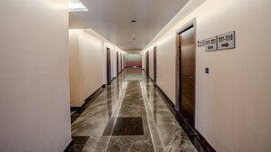 A long, well-lit hallway with marble flooring, wooden doors, and directional signs on the walls. - HOTEL LUCKY INDIA  (Bhubaneshwar)