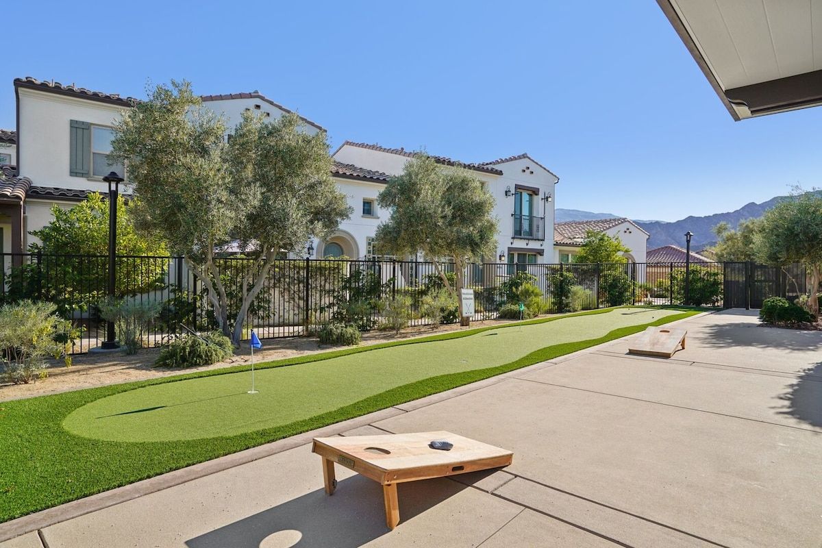 A residential area with a well-maintained lawn, a wooden board game table, and a house with a tiled roof.