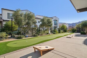 A residential area with a well-maintained lawn, a wooden board game table, and a house with a tiled roof.