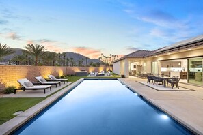 A swimming pool with lounge chairs and a patio area with a table and chairs. - Vista Santa Rosa: Pool, Firepit, BBQ, EV Charger (La Quinta)