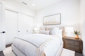 A bedroom with a large bed, bedside tables, a door, and a wall-mounted artwork.