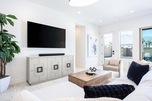 A modern living room with a flat-screen TV, a light-colored cabinet, a coffee table, and a sofa with decorative pillows.