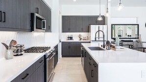 A modern kitchen with dark cabinetry, a central island, and pendant lighting.