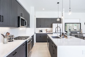 A modern kitchen with dark cabinetry, a central island, and pendant lighting.