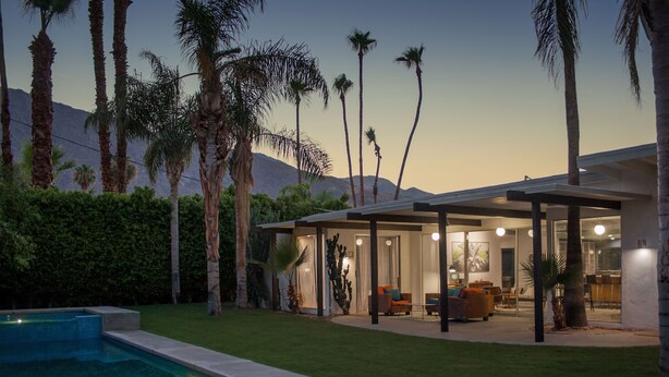 A modern house with a swimming pool, outdoor seating area, and a view of mountains.