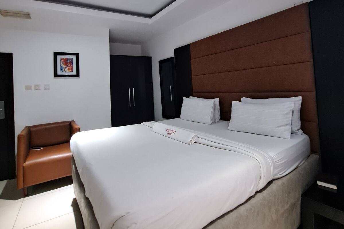 A modern hotel room with a large bed, a brown leather chair, and a framed picture on the wall.