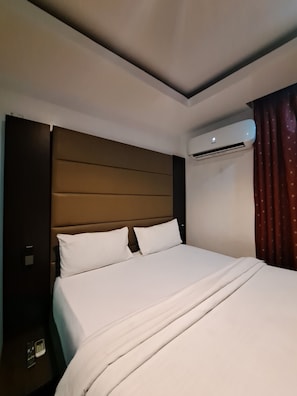 A hotel room with a large bed, a headboard, an air conditioning unit, and a curtain. - Axor Hotel &Suites  (Lekki)