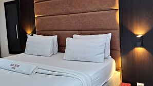 Un letto rifatto con lenzuola bianche, una testiera imbottita marrone e due abat-jour.