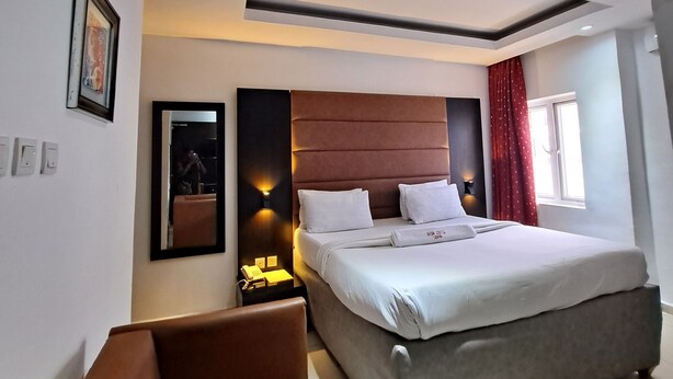 Una moderna camera d'albergo con un letto grande, un comodino con una lampada, un piccolo angolo salotto e una finestra con tende.