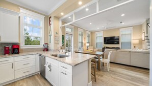 A spacious kitchen with a large island, white cabinetry, and a dining area with a sofa and TV. - Charming 3BR Home on 30A – Golf Cart Included, 5 Min to Beach (Santa Rosa Beach)