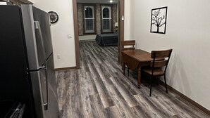 A kitchen with a refrigerator, wooden flooring, and a dining area with a table and chairs.
