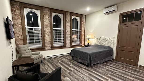 A bedroom with a bed, a chair, a TV, and a window with blinds.