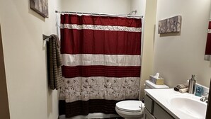 A bathroom with a shower curtain, toilet, sink, and wooden flooring.
