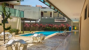 A poolside area with lounge chairs and a swimming pool, surrounded by buildings and a clear sky. - Manawa Beach Flat by All (Ipojuca)
