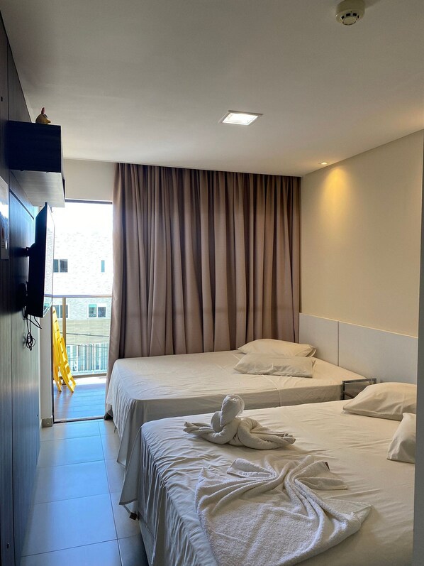 A hotel room with two beds, a TV mounted on the wall, and a balcony with a yellow chair.