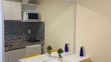 Cocina compacta con microondas, pileta y salpicadero de azulejos. Posee una pequeña mesa de comedor con dos sillas amarillas y dos plantas en macetas.