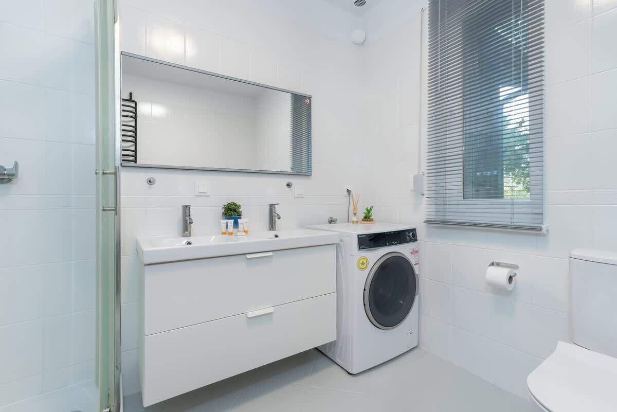 Un baño moderno con lavamanos, espejo y inodoro blancos.