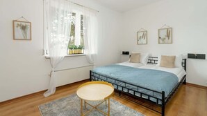 Ein Schlafzimmer mit einem Bett, einem kleinen runden Tisch und einem Fenster mit durchsichtigen Vorhängen.