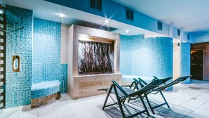 Un moderno espacio de spa con pared de azulejos azules, banca de madera y fuente de agua.