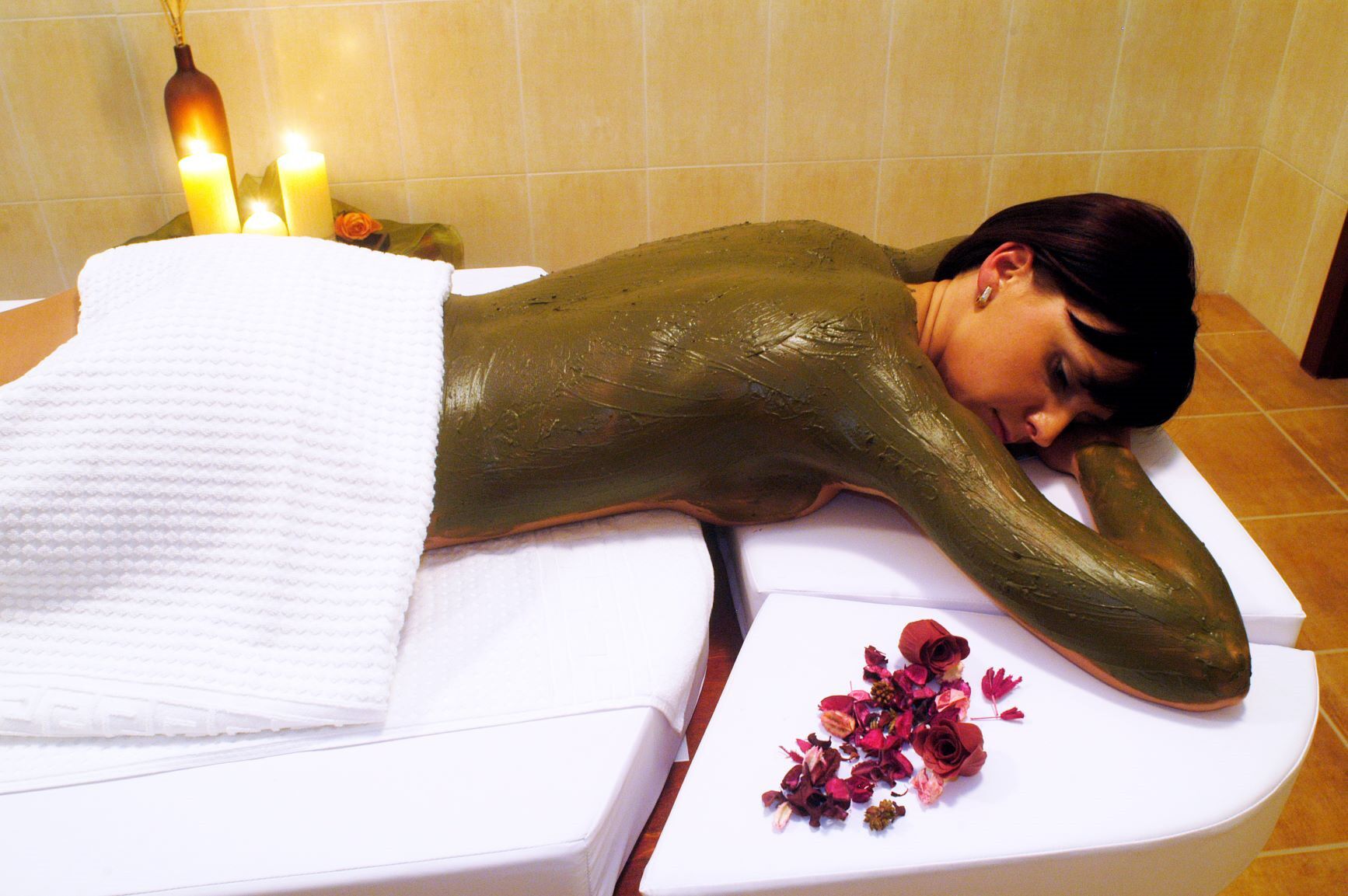 A person receiving a massage in a room with candles and dried flowers on the table.