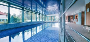 An indoor swimming pool with clear glass walls, a tiled floor, and a view of trees outside. - Hotel Alma MED & SPA - UWAGA - styczen do marzec 2026 basen nieczynny! (Barlinek)