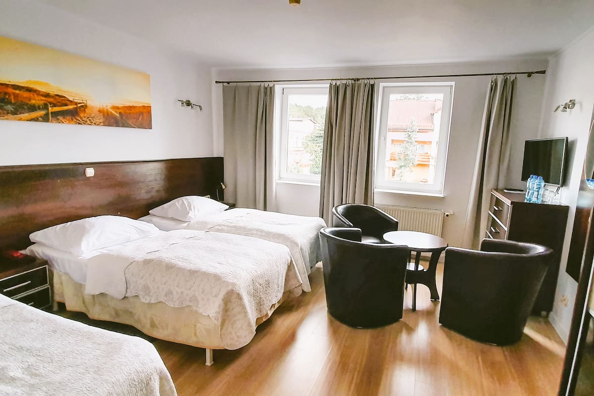 A hotel room with two beds, a desk with a chair, a TV, and a painting on the wall.