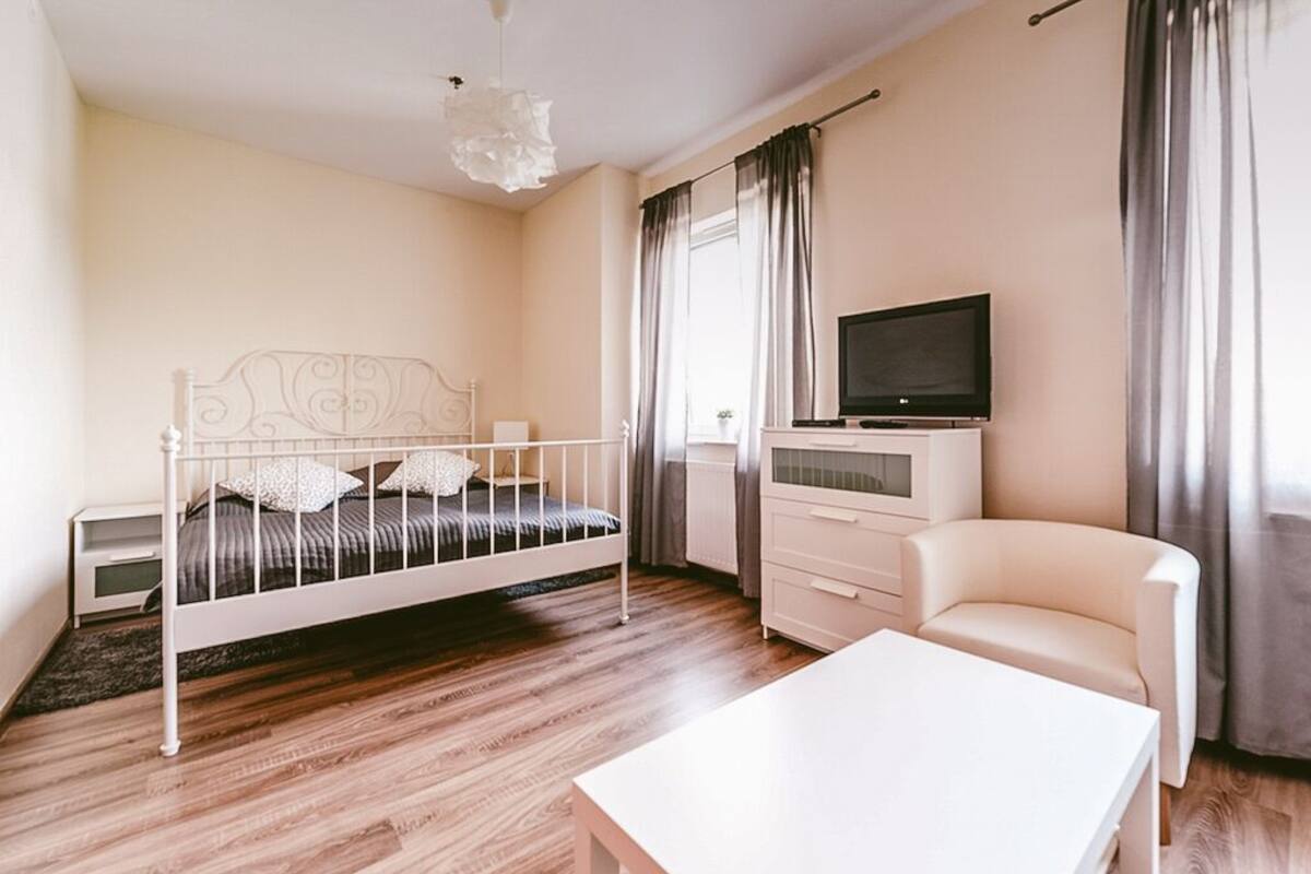 A bedroom with a white metal bed, a television on a dresser, a white chair, and a wooden floor.