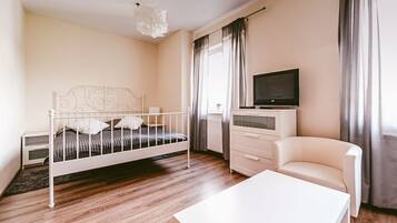 Una camera da letto con un letto in metallo bianco, una televisione su un comò, una sedia bianca e un pavimento in legno.