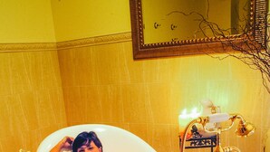 Una bañera con un grifo dorado y una flor en el suelo.