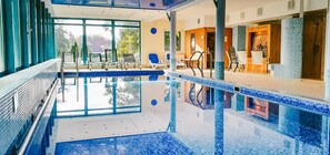A modern indoor swimming pool with clear glass walls, blue-tiled pool, and sunlit seating area. - Hotel Alma MED & SPA - UWAGA - styczen do marzec 2026 basen nieczynny! (Barlinek)