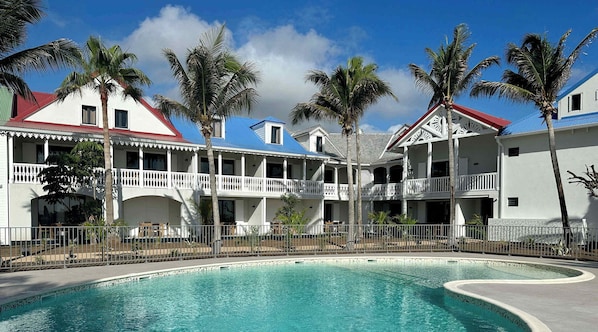 A resort with a swimming pool, multiple-story buildings with balconies, and palm trees.