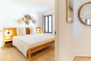 A bedroom with a wooden bed, bedside lamps, a wall-mounted mirror, and a window with curtains.