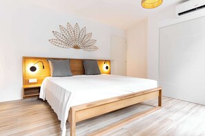 Ein modernes Schlafzimmer mit einem Holzbett, zwei Nachttischlampen, einer Wanddekoration aus Blättern und einer weißen Tür.