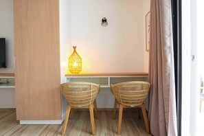 A room with a wooden floor, two wicker chairs, a desk with a lamp, and a television on the left.
