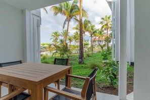 A wooden table and chairs in a covered outdoor area with a view of palm trees and a building in the background.