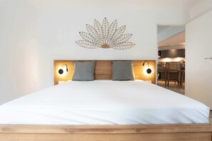 A neatly made bed with a wooden headboard, two wall-mounted reading lights, and a decorative wall piece above the bed.