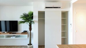 A modern living room with a flat-screen TV, a wooden coffee table, a potted plant, a built-in white shelving unit, and a white wardrobe with a partially open door.