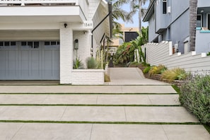 A residential street with a white house numbered 1349, a garage, and a paved driveway with grass edging.