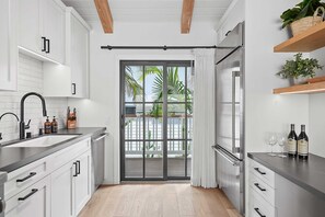 A modern kitchen with white cabinets, a black countertop, and a sliding glass door leading to a balcony with a view of palm trees.