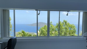 A room with a large window offering a view of the sea and a distant island.